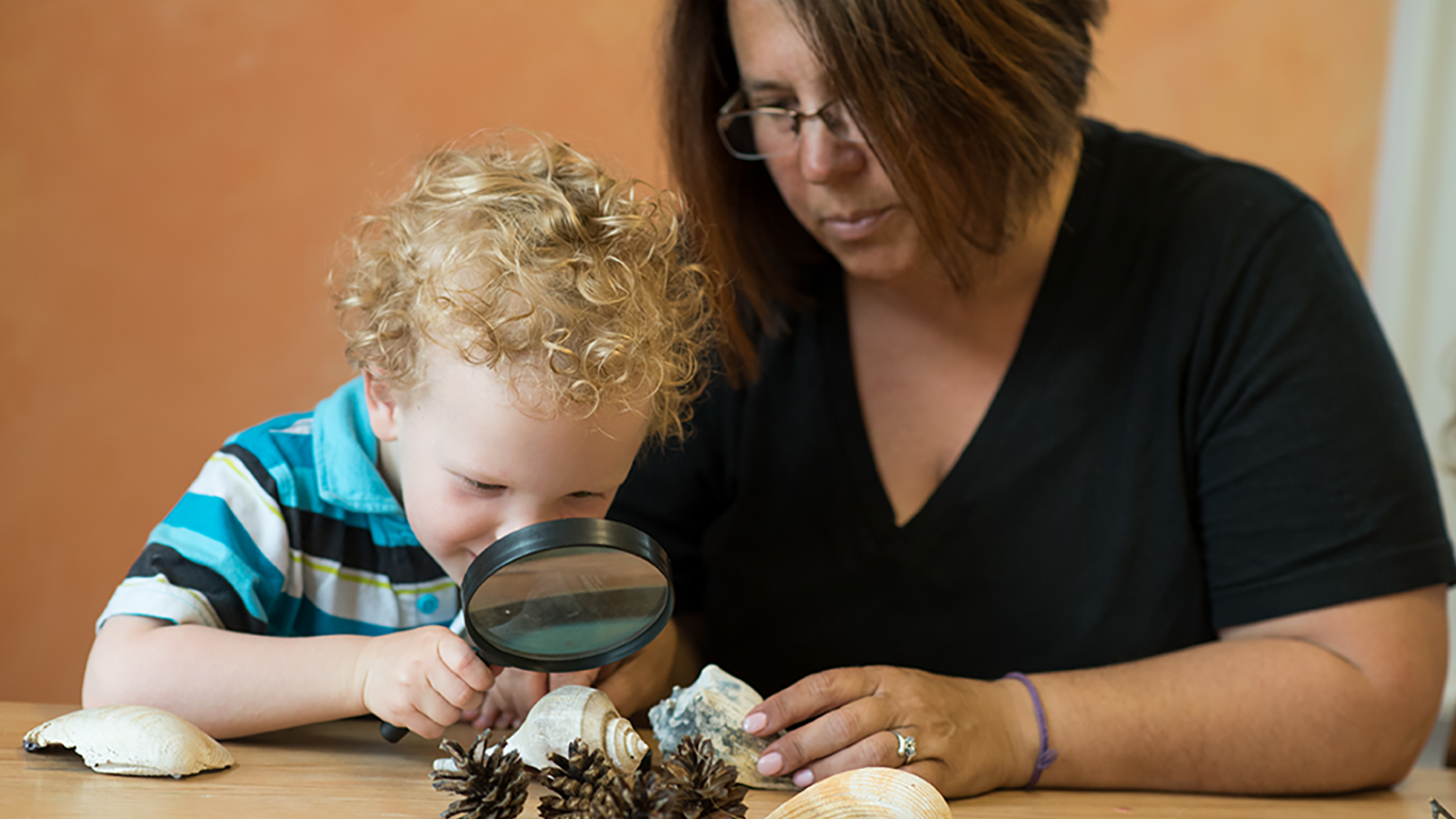 Teacher with young student looking in magnifying glass at shells