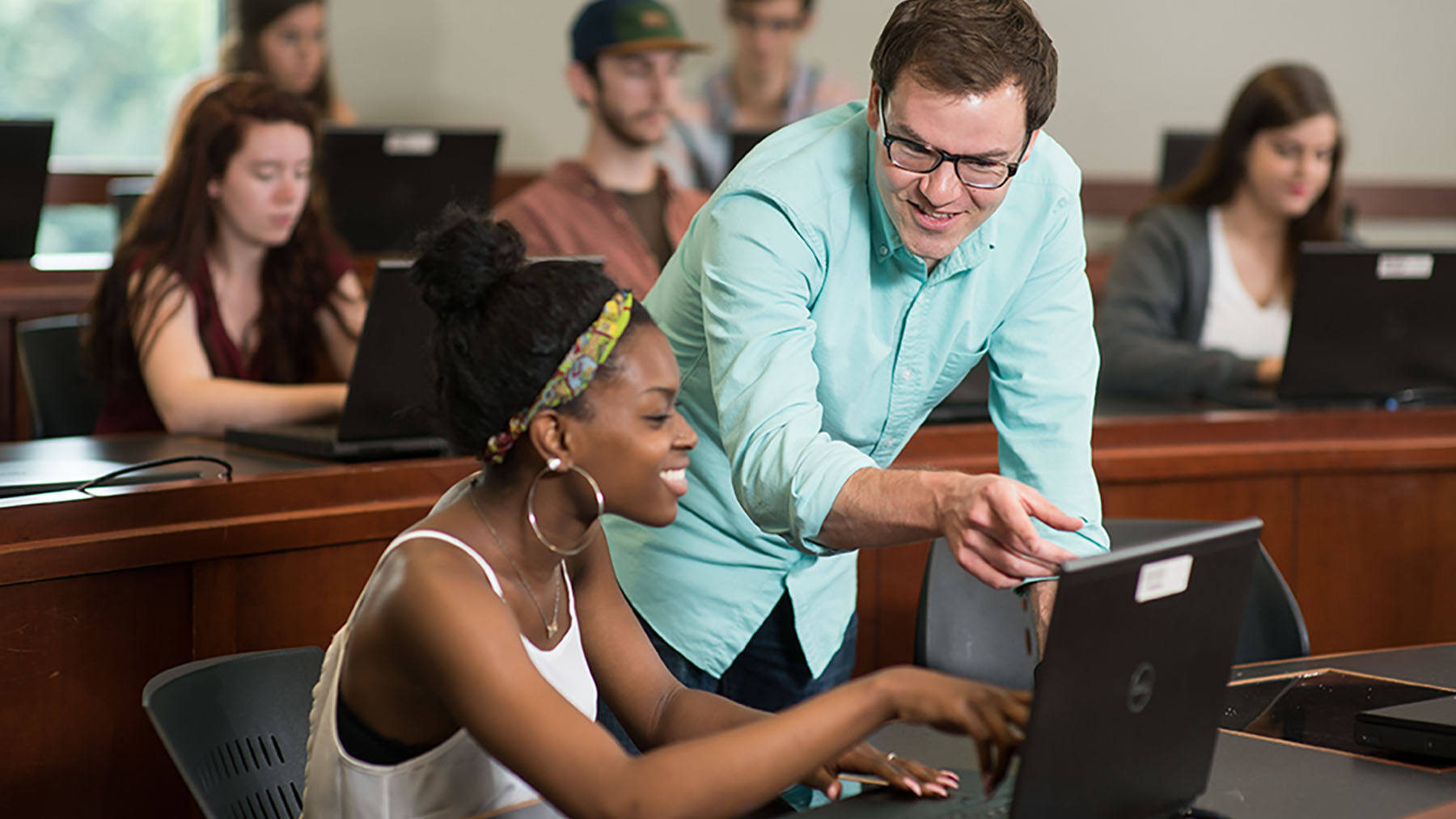 Teacher helping a student at a laptop in classroom