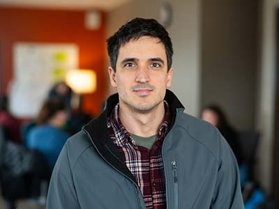 Italian looking male with dark hair and a plaid shirt looking at camera