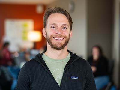 White adult male with beard and mustache dressed in green tshirt and a zip up sweater
